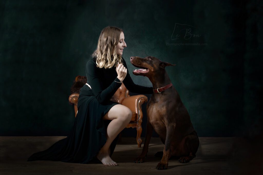 jeune femme assise a coté d'un fauteuil marron en cuir avec un chien dobermann assis a coté d'elle et se regarde