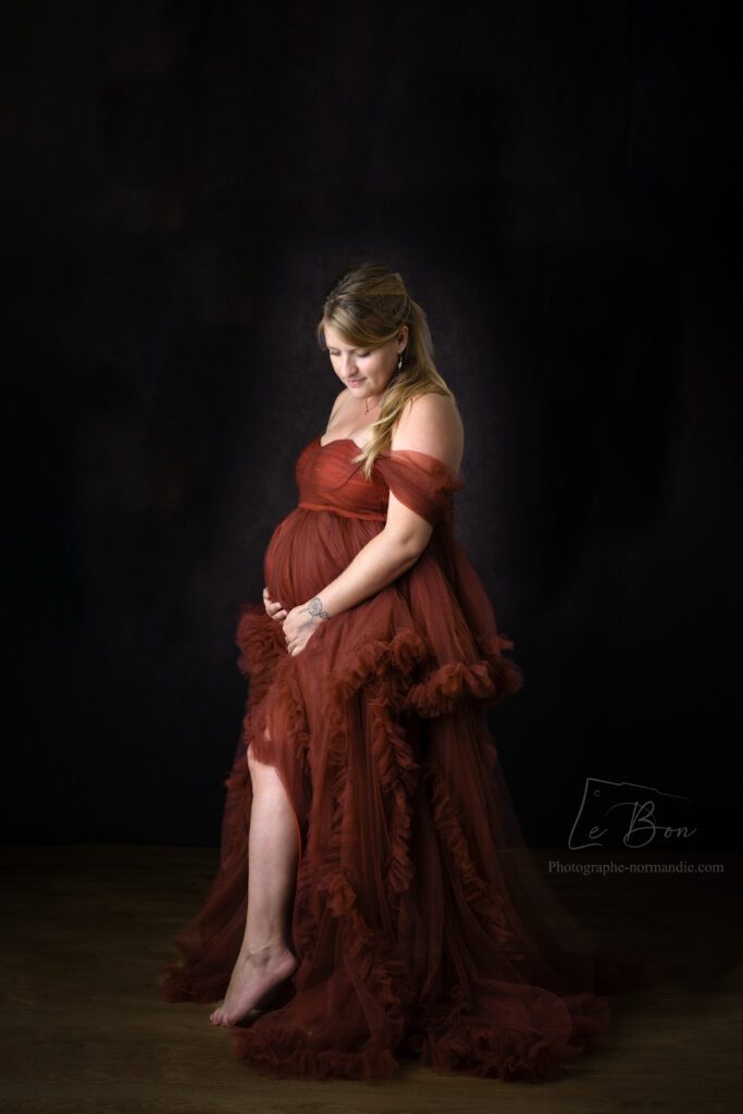 femme enceinte blonde en robe rouge dans un studio photo sur fond marron 